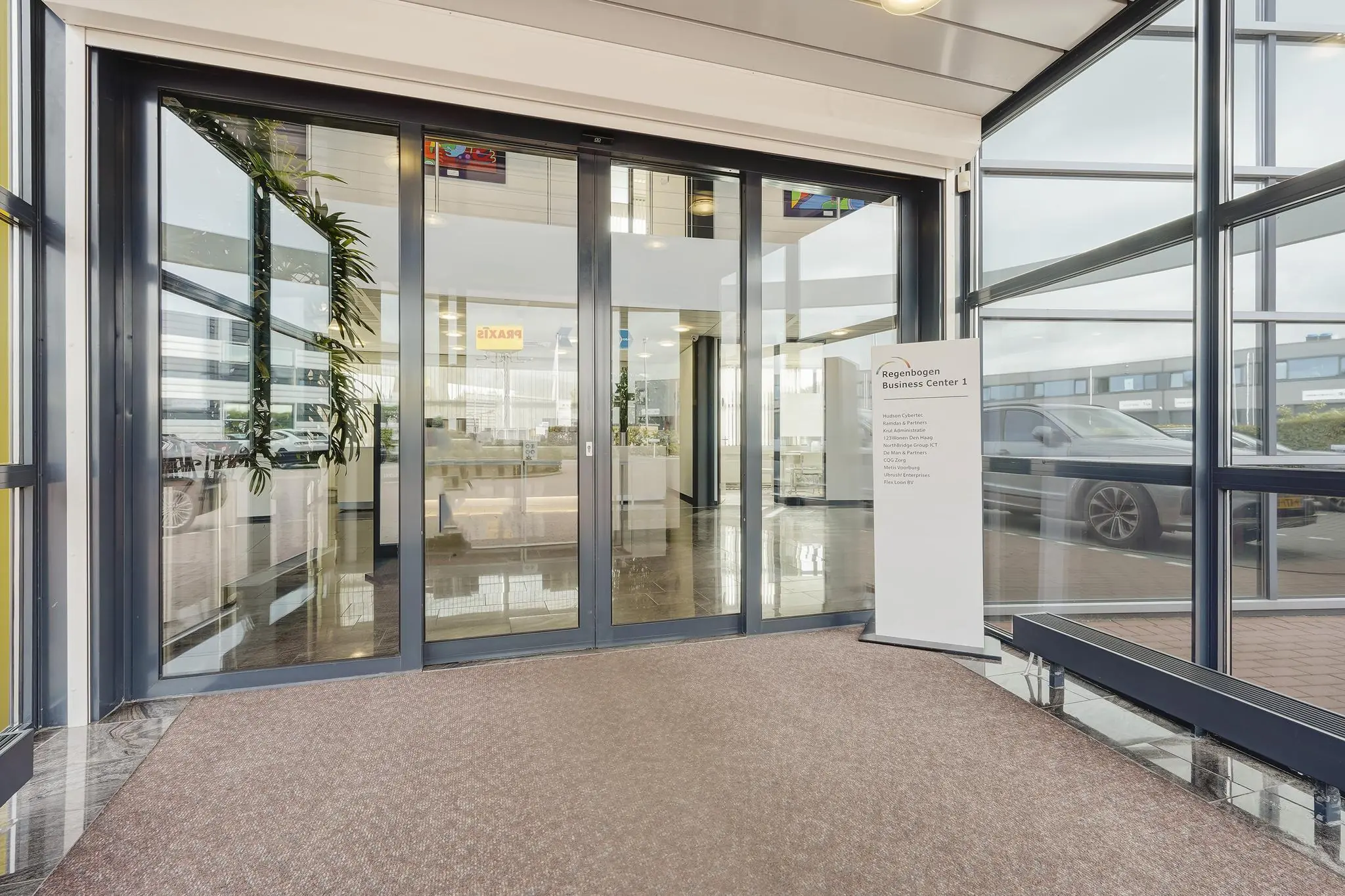 Ingang van Regenbogen Business Center 1 aan de Laan van 's-Gravenmade met schuifdeuren en een informatiebord.